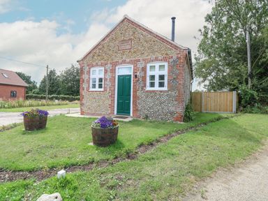 A small stone and brick building with a green door and two windows in a grassy area with flower pots at Wensum Spring Horningtoft near Fakenham