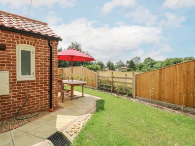 A backyard with a brick house wall a wooden table with chairs and a red umbrella and a wooden fence in the background at Wensum Spring in Horningtoft near Fakenham