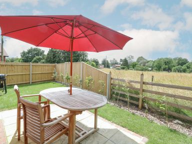A patio with wooden table and chairs with a red umbrella in a garden at Wensum Spring Horningtoft near Fakenham
