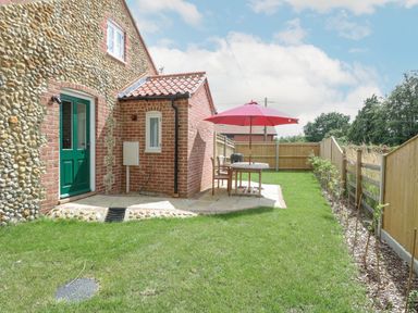 An outdoor patio with a table, chairs, and a red umbrella next to a brick and stone house at Wensum Spring Horningtoft near Fakenham