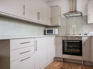 A kitchen with white cabinets a built in oven a microwave and a stainless steel extractor hood at Ostlers in Mitcheldean