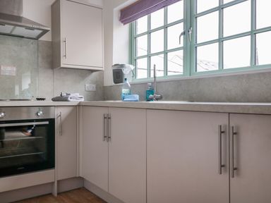 A kitchen with built in oven sink and gray cabinets under a green framed window at Ostlers in Mitcheldean