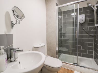 A bathroom with a sink a toilet a wall-mounted mirror and a shower enclosure with gray tiles at Ostlers in Mitcheldean