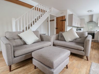 A living area with two sofas a matching ottoman and a staircase in the background at Ostlers in Mitcheldean