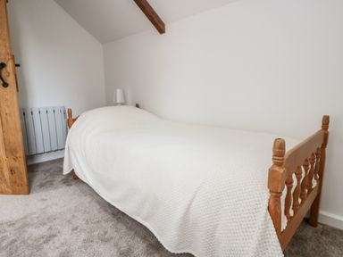 A small bedroom with a single wooden bed covered by a white blanket a wooden door and a white lamp on a bedside table at Ostlers in Mitcheldean