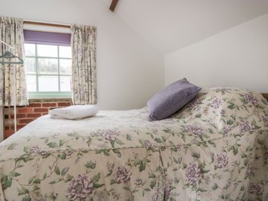 A bedroom with a bed covered in floral bedspread and a window with floral curtains at Ostlers in Mitcheldean
