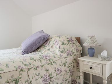 A bedroom with a floral bedspread and a bedside table with a lamp and tissues at Ostlers in Mitcheldean