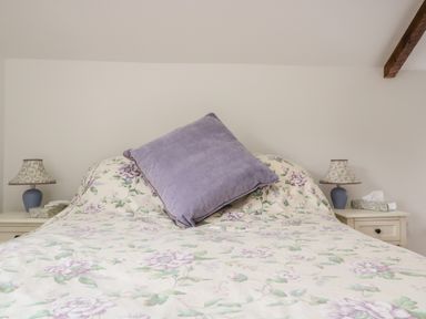 A bed with floral bedspread and a purple pillow with two bedside tables with lamps and tissue boxes at Ostlers in Mitcheldean