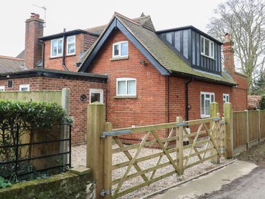 A brick house with multiple windows and two chimneys behind a wooden gate and fence at The Lodge in Wroxham