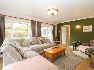 A living room with sofas a wooden coffee table and large windows at The Lodge in Wroxham