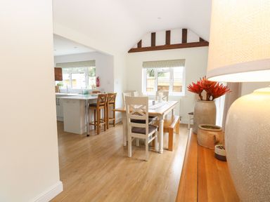 A dining area with a wooden table and chairs next to a kitchen with bar stools at The Lodge in Wroxham