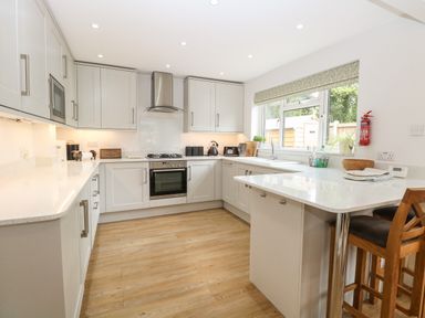 A kitchen with white cabinets wooden floor a countertop with two wooden stools and a window at The Lodge in Wroxham