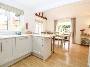 A kitchen with white cabinets and a dining area with a wooden table and chairs at The Lodge in Wroxham