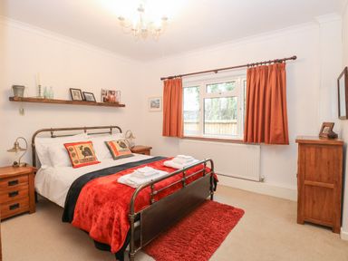 A bedroom with a metal bed frame red and black bedding two wooden bedside tables a wooden dresser and red curtains at The Lodge in Wroxham