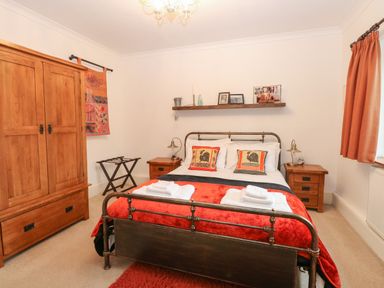 A bedroom with a double bed with red bedding and two bedside tables at The Lodge in Wroxham