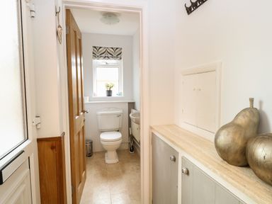 A small bathroom with a toilet and window and a hallway with cabinets and decorative metallic fruit at The Lodge in Wroxham
