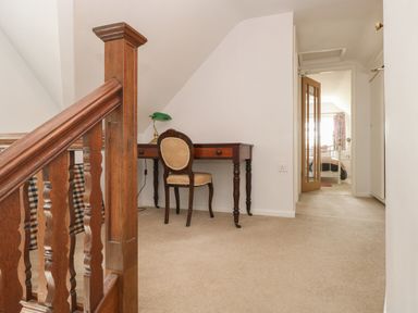 A hallway with a wooden staircase, a wooden desk with a chair and a lamp, and a bedroom visible through an open door at The Lodge in Wroxham
