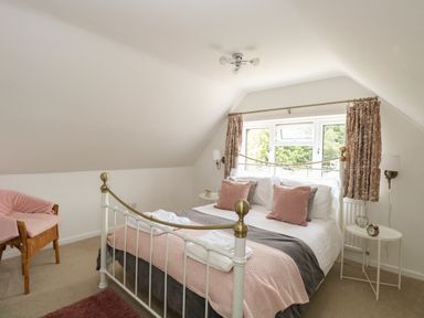 A bedroom with a bed pillows and windows with curtains and a chair at The Lodge in Wroxham