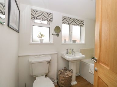 A bathroom with a toilet sink bathtub two windows with patterned blinds and a wicker basket at The Lodge in Wroxham