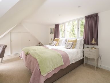 A bedroom with a double bed green and pink bedding bedside tables with lamps and windows with curtains at The Lodge in Wroxham