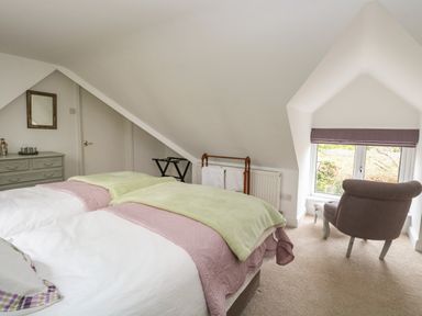A bedroom with a double bed a gray dresser a chair by the window and a towel rack at The Lodge in Wroxham