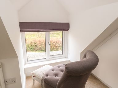 A room corner with a window, a gray armchair, and a small white footstool at The Lodge in Wroxham