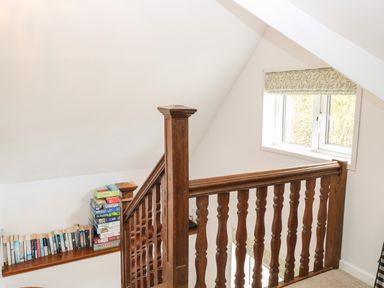 A wooden staircase railing with books and board games stacked on a shelf under a window with patterned blinds at The Lodge in Wroxham