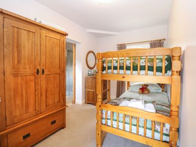 A bedroom with wooden bunk beds a wooden wardrobe and a small wooden cabinet with a mirror on the wall at The Lodge in Wroxham
