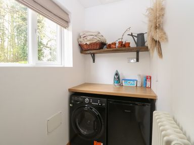 A laundry room with a washing machine a dryer a wooden countertop an iron and cleaning supplies on the counter and a wooden shelf with a basket and pots at The Lodge in Wroxham