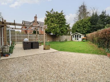 A backyard with a gravel area patio with furniture a grassy lawn a tree a small shed and a wooden fence at The Lodge in Wroxham