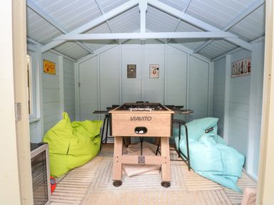 A room with a foosball table in the center two bean bags on each side and posters on the walls at The Lodge in Wroxham