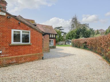 A gravel driveway beside a brick house with a hedge and garden shed at The Lodge in Wroxham