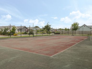 An outdoor tennis court with net fencing and residential houses in the background at Driftwood Filey