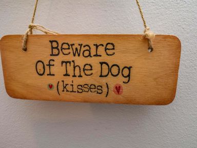 A wooden sign with the text 'Beware Of The Dog (kisses)'