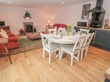 An open plan living and dining room with a round dining table set for six near a kitchen area with black cabinets and a stove at Todridge Barn in Corbridge