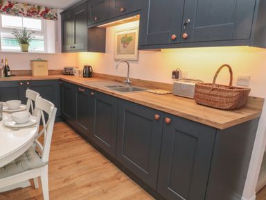 A kitchen with dark cabinets wooden countertop and a dining table with white chairs at Todridge Barn in Corbridge