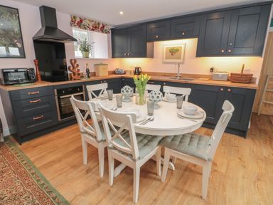 A kitchen with dark cabinets wooden countertops a round dining table with six chairs and table settings at Todridge Barn in Corbridge