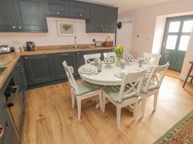 A kitchen with blue cabinets a wooden countertop a white round dining table set with six chairs and a vase of yellow flowers at Todridge Barn in Corbridge