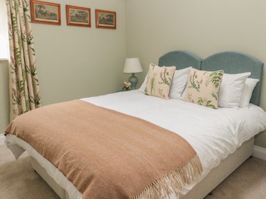 A bedroom with a bed with a brown throw and floral cushions a lamp on a bedside table and framed pictures on the wall at Todridge Barn in Corbridge