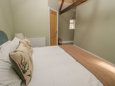 A bedroom with a bed and floral pillows a wooden door and a small window at Todridge Barn in Corbridge
