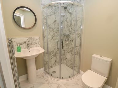 A bathroom with a shower enclosure a pedestal sink with a round mirror and a toilet at Todridge Barn in Corbridge