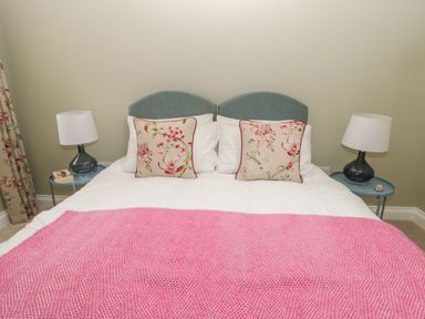 A bed with two floral pillows white bedding and a pink blanket with bedside tables and lamps at Todridge Barn in Corbridge