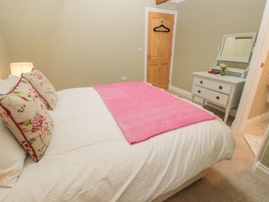 A bedroom with a double bed with floral pillows and a pink blanket and a white dresser with a mirror and door at Todridge Barn in Corbridge