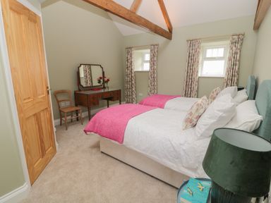 A bedroom with twin beds pink throws wooden door a dressing table with mirror and a chair at Todridge Barn in Corbridge