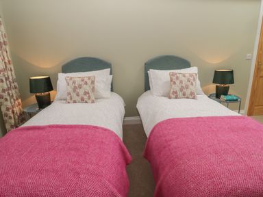 A bedroom with two single beds with pink blankets and floral pillows at Todridge Barn in Corbridge