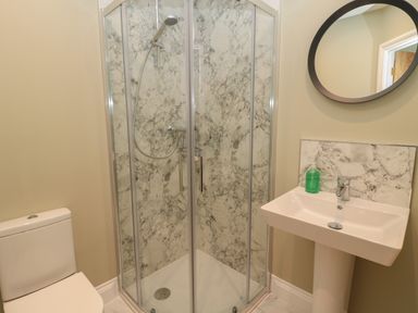 A bathroom with a toilet shower enclosure with glass doors pedestal sink and round mirror at Todridge Barn in Corbridge