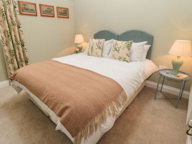 A bedroom with a bed with floral pillows a brown blanket bedside tables with lamps and framed pictures on the wall at Todridge Barn in Corbridge