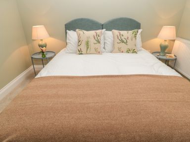 A double bed with white bedding floral pillows and a brown blanket with bedside tables and lamps at Todridge Barn in Corbridge