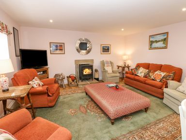 A living room with orange sofas and armchairs a patterned ottoman a fireplace and a television at Todridge Barn in Corbridge
