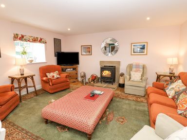 A living room with orange armchairs a patterned ottoman green rug and a fireplace at Todridge Barn in Corbridge